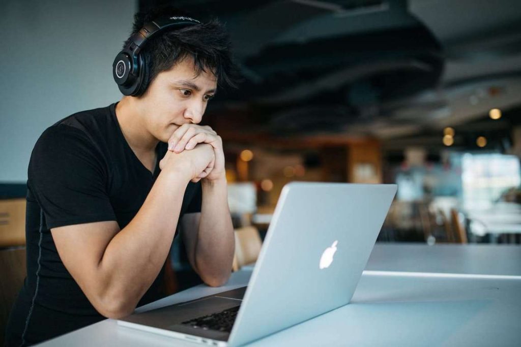 A man wearing a pair of headphones and looking at the laptop screen.