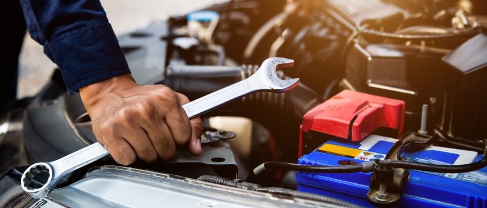 man holding a spanner working on car battery